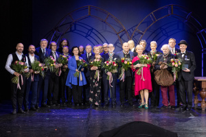 W pomieszczeniu stoją osoby odznaczone medalami Gloria Artis. Każda z nich ma zawieszony bądź przypięty do ubrania medal Gloria Artis i trzyma bukiet kolorowych kwiatów, Uśmiechają się. Wśród osób, z lewej strony zdjęcia, znajduje się profesor Wydziału Scenografii - pan Marek Chowaniec.